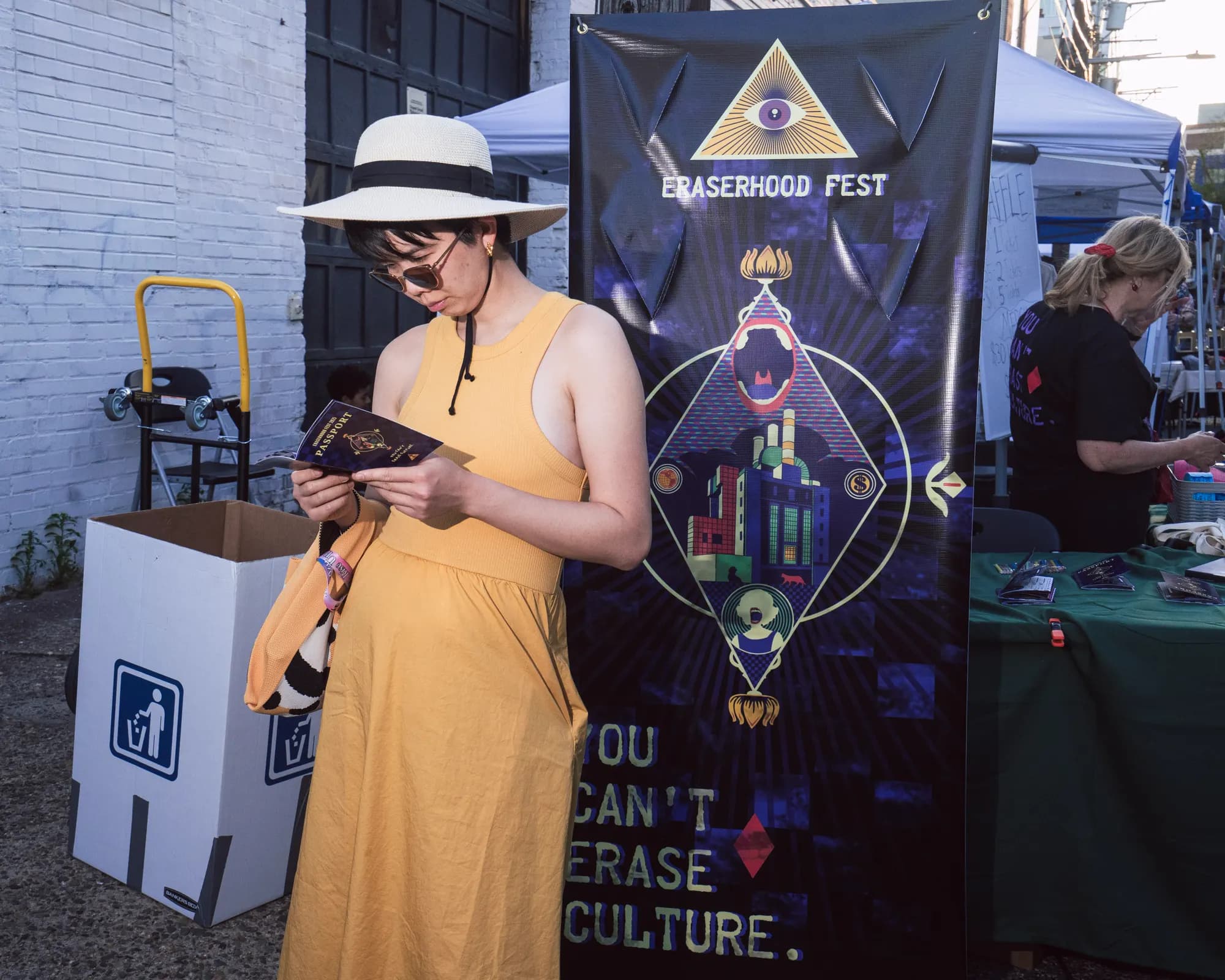 A festivalgoer in a wide-brimmed hat beside the banner reading You Can't Erase Culture.