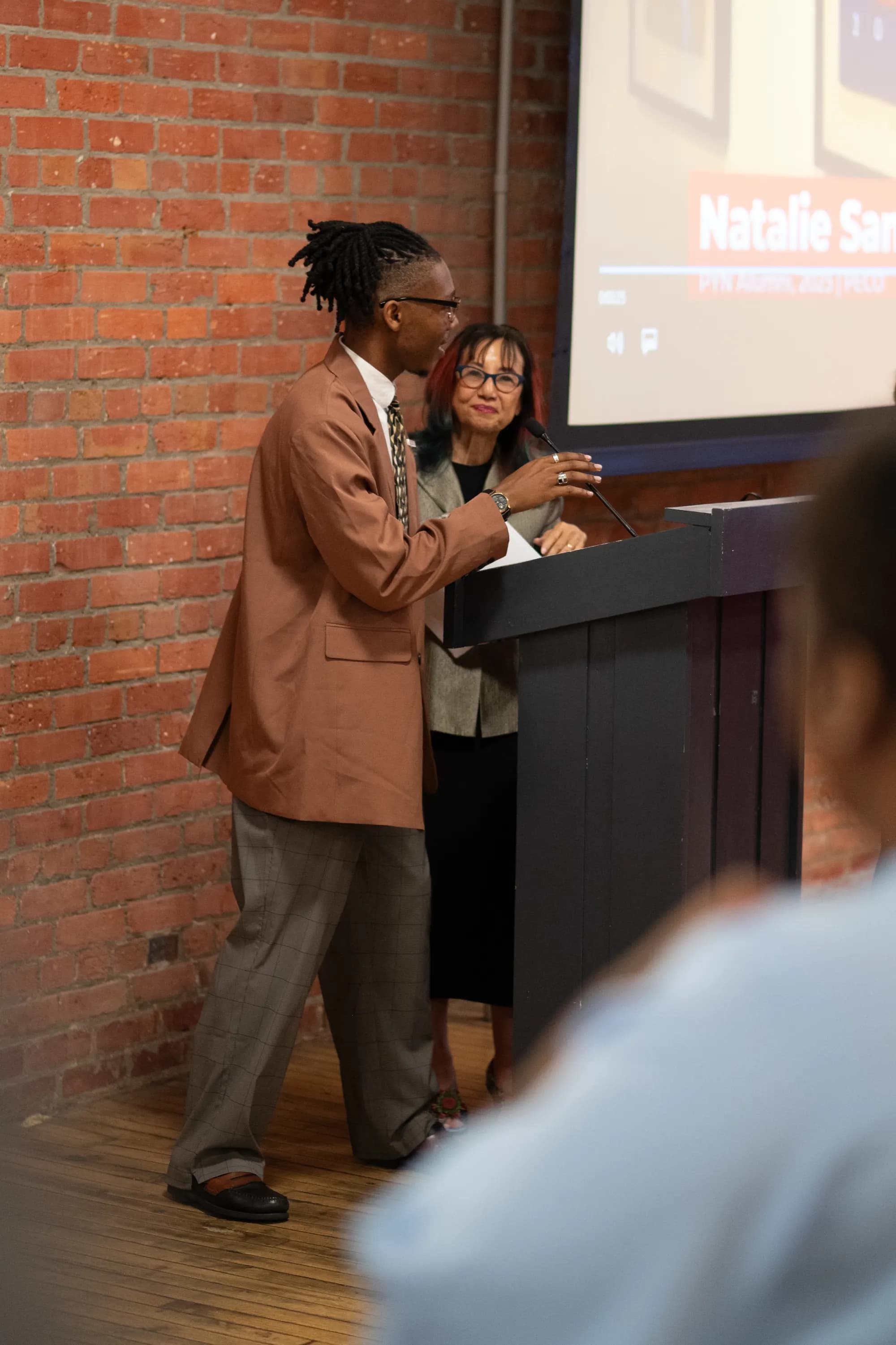 A speaker at the podium beside a presentation screen.