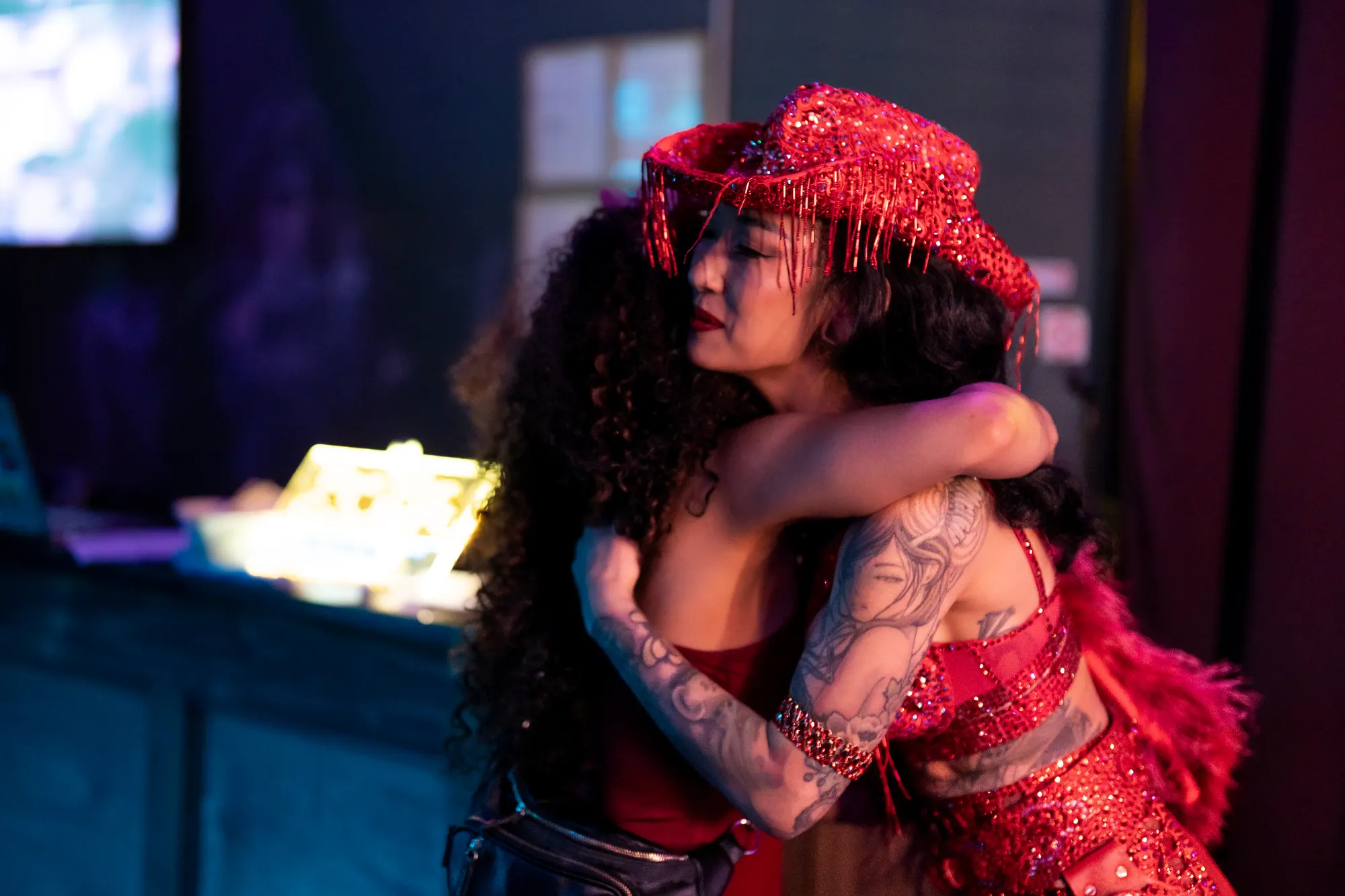 A performer in a red sequined costume and veil holding an embrace on stage.
