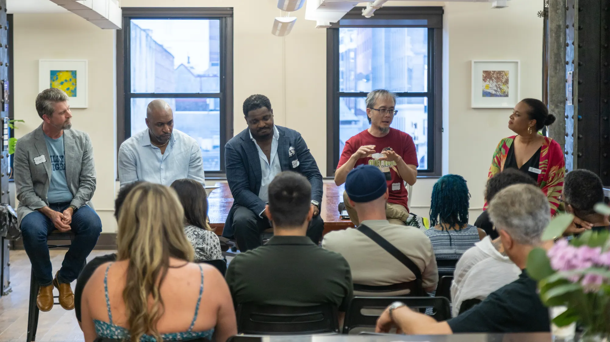 A five-person panel seated at the front of the loft, one speaker mid-sentence, the audience filling the rows in front.