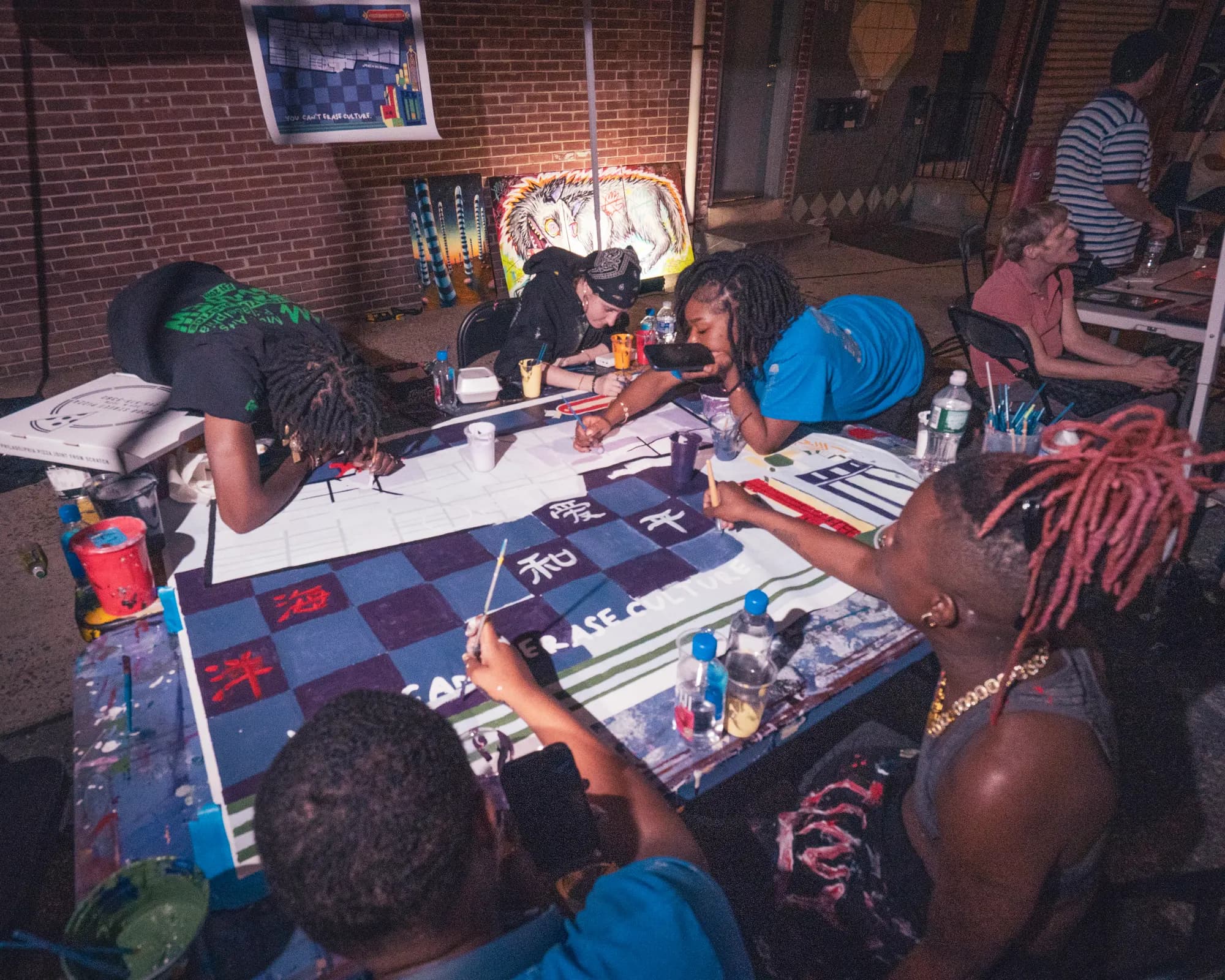 Artists at work around a table in a dim tattoo and art studio.