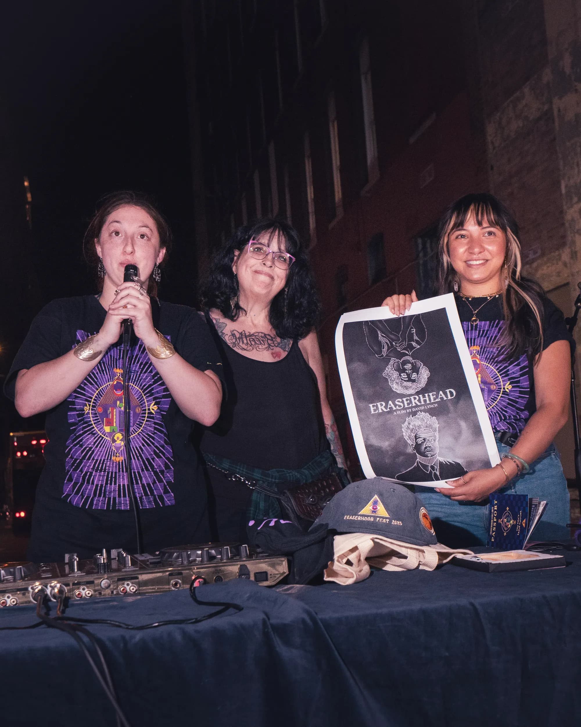 Three organizers at the merch table holding up an Eraserhead print.