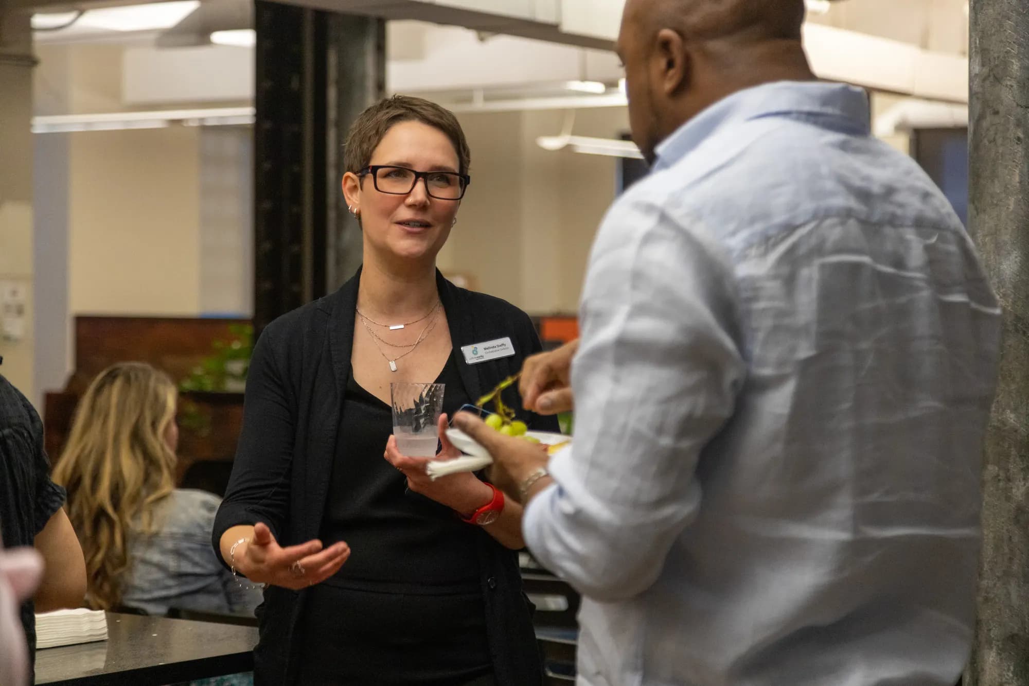 Two attendees talking over drinks, name tags on, after the panel.