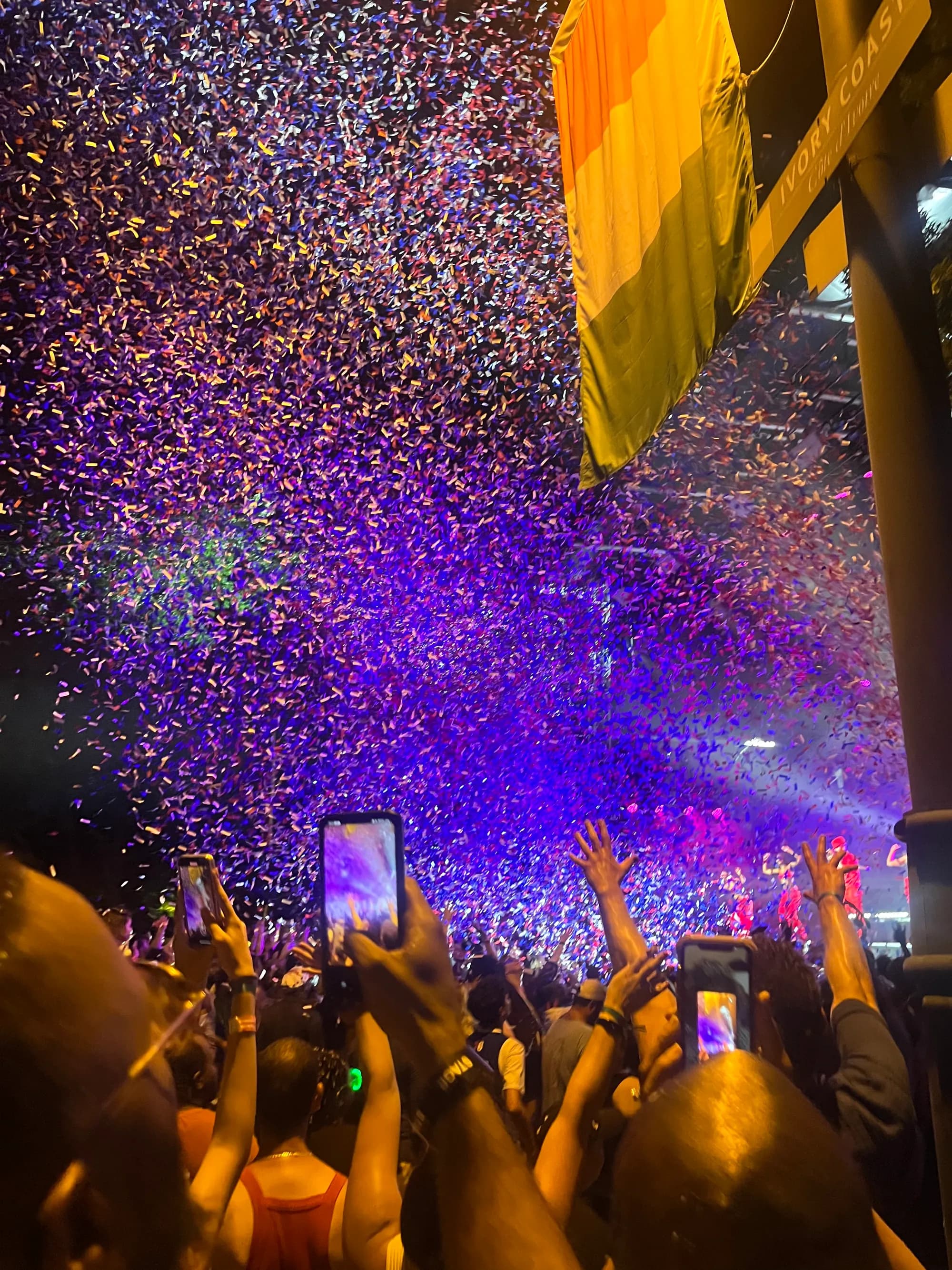 Confetti pouring over the crowd at the night show, phones raised toward the stage in purple light.