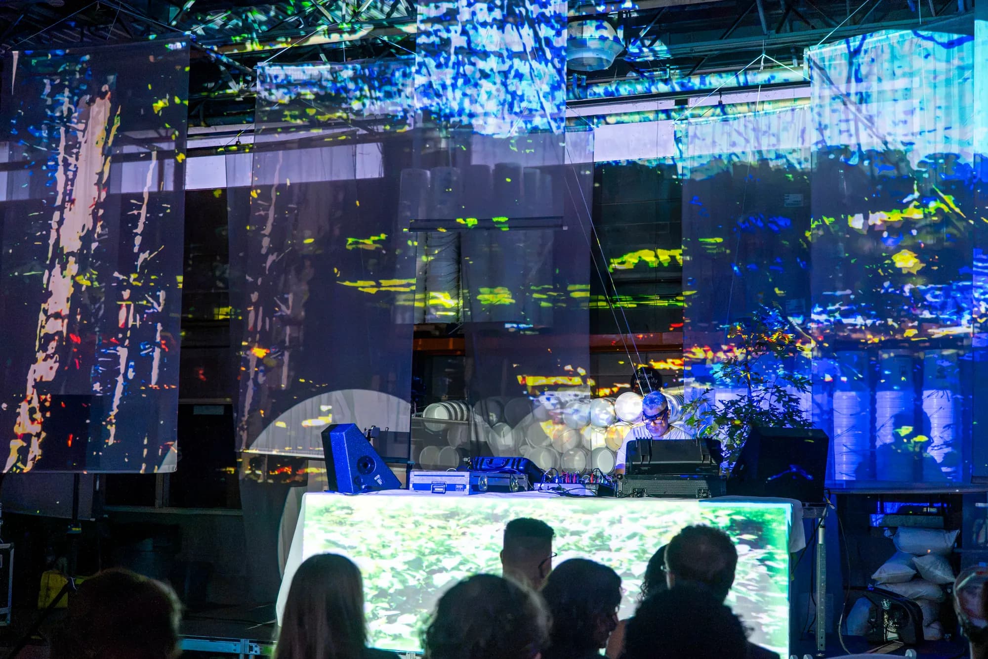 Projection-mapped visuals washing across a warehouse wall above a seated audience.