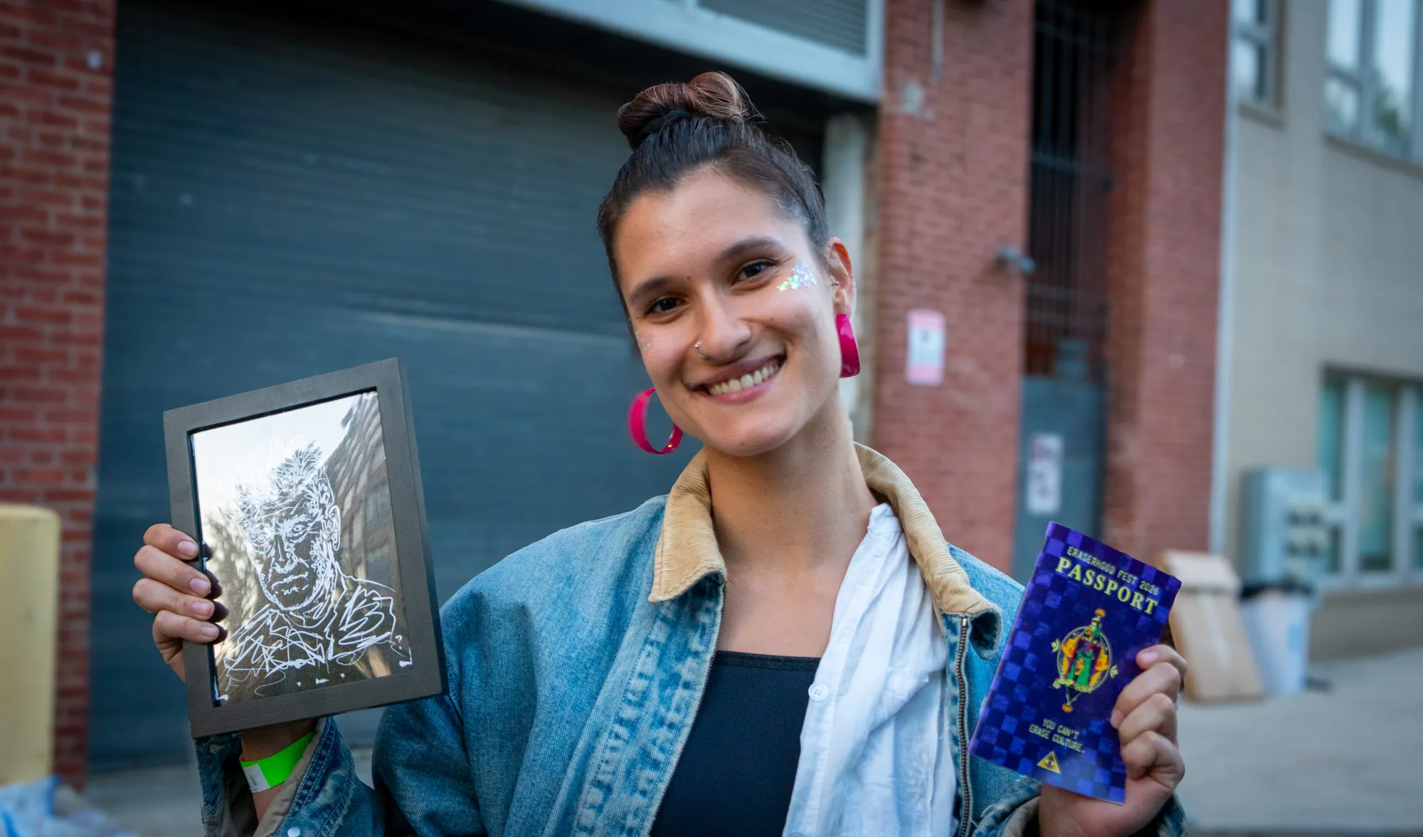 A festivalgoer smiling with a framed print in one hand and her Eraserhood Fest passport in the other.