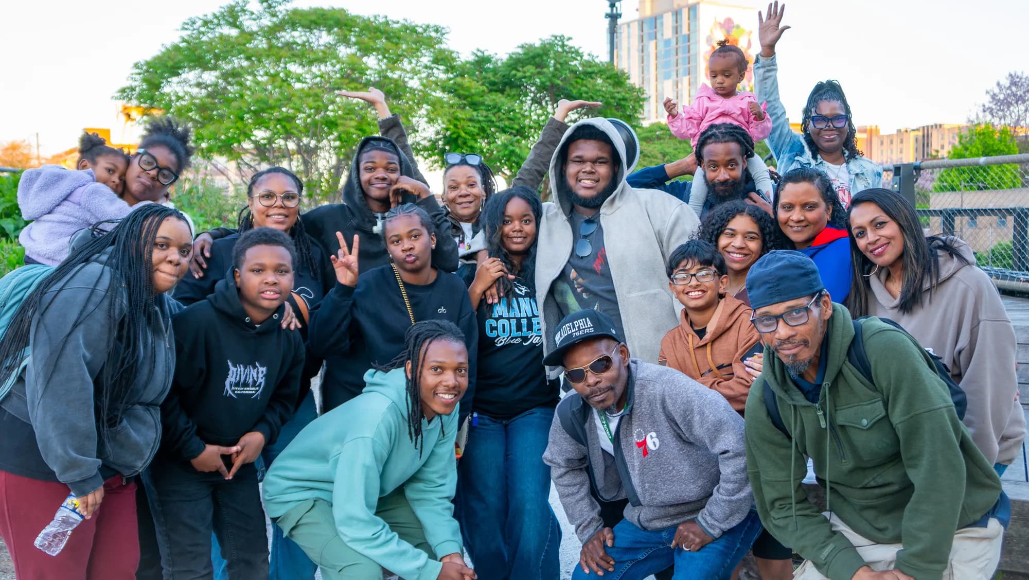 A large group packed together for a photo in the park, hands raised.